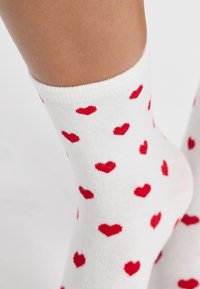 Calzini bianchi in cotone con un motivo ripetuto di piccoli cuori rossi, con un bordo a coste e una texture liscia.