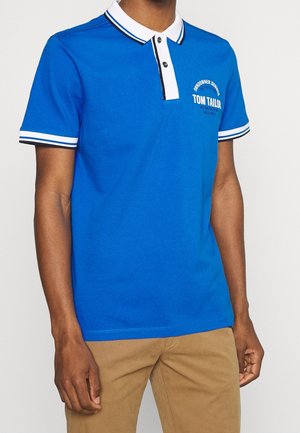Niebieska koszulka polo z białym kołnierzykiem i paskowymi detalami. Posiada dwa guziki i logo na piersi. Miękka bawełniana tkanina, casualowy krój.