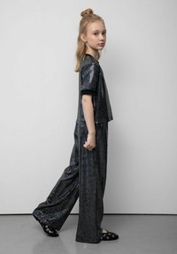 Czarna bluzka z cekinami i spodnie o szerokich nogawkach, oba elementy o błyszczącej fakturze. Strój obejmuje czarny kołnierz i luźny krój. Czarne wsuwane buty z akcentami.
