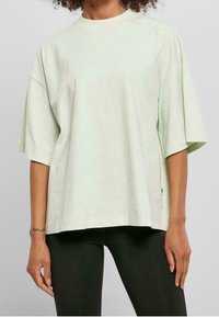 Světle zelené oversized tričko vyrobené z měkké bavlny, s kulatým výstřihem, spadlými rameny a krátkými rukávy. Jemná značka na lemu.