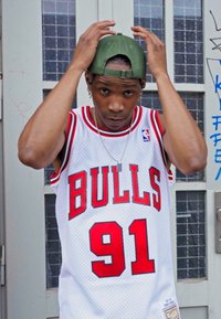 Tricou de baschet alb cu litere roșii "BULLS", numărul "91" și accente negre. Căciulă verde și lanț de argint cu straturi. Fundal gri.