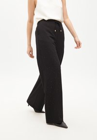 Čierne široké nohavice s viazačkou v páse, s malými striebornými ozdobami a hladkým povrchom. V kombinácii s čiernymi špicatými opätkami.