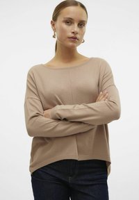 Pull en tricot beige avec un col rond, des épaules dénudées et une finition texturée. Présente un ourlet arrière légèrement plus long et des poignets côtelés.