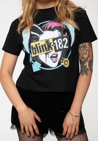 Black cropped t-shirt featuring a colorful graphic design of a stylized face with pink hair and "blink-182" text. Soft cotton material.