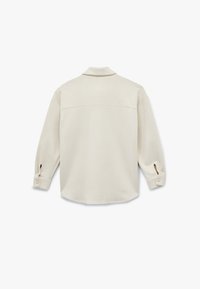 Lys beige langærmet skjorte med krave, rygkotelet detalje og knappede manchetter med udskæringsdetaljer ved ærmeåbningerne.
