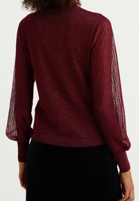 Bordeauxfärgad tröja med ribbat stickat material och genomskinliga, plisserade ärmar. Mjuk textur med en subtil lyster. Figursydd design med hög hals.