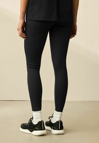 Sorte ribbede leggings lavet af strækbart materiale, parret med sorte træningssko og hvide sokker, placeret mod en neutral baggrund.