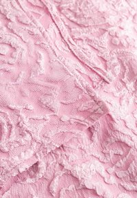 Textured pink fabric featuring intricate raised rose patterns, soft finish, and subtle sheen with visible stitching details.