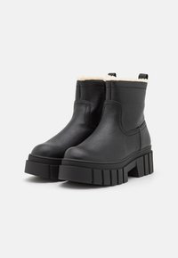 Bottines noires en cuir avec une semelle épaisse et texturée, dotées d'une doublure en fausse fourrure douce le long du bord supérieur.