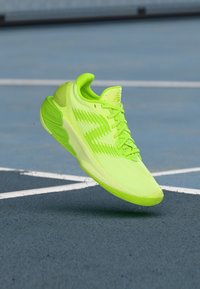 Scarpa da atletica verde neon con una tomaia leggera in rete, dettagli testurizzati e suola in gomma, progettata per offrire trazione su diverse superfici.