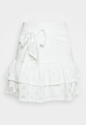 Falda de tela blanca con ojales, con volantes en capas y un gran lazo atado en la cintura, con patrones florales recortados.