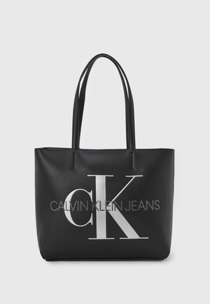 Czarna torba typu tote Calvin Klein z długimi uszami i dużym srebrnym logo "CK" oraz napisem "Calvin Klein Jeans" z przodu.