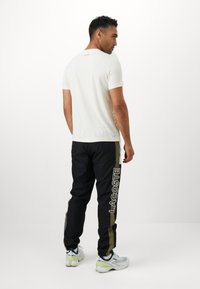 Hvit kortermet t-skjorte og svarte joggebukser med grønne side-striper og "LACOSTE" logo. Treningssko med hvite, blå og grønne detaljer.