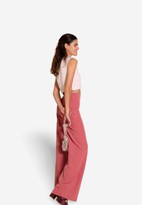 Haut court rose pâle et pantalon taille haute blush, associés à une pochette métallique et des chaussures à talons bourgogne. Modèle de profil.