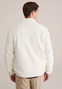 Pullover bianco in pile con colletto alto, superficie texturizzata e vestibilità rilassata. Presenta polsini elasticizzati e orlo dritto.