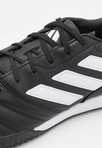 Svarta syntetiska sportskor med vita diagonala ränder, med en strukturerad läderyta, svarta snören och en mönstrad gummisula.