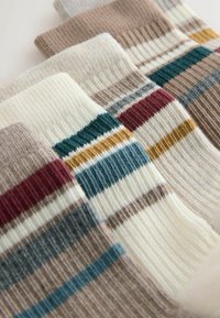 Monivärisiä sukkia, joissa on ribbitetty pinta. Keskellä on teal-, viininpunaisia, sinapinvärisiä, harmaita ja ruskeita raitoja kerma- ja vaaleanbeige-taustalla.
