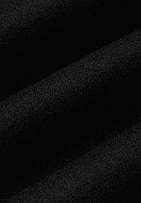 Czarna tkanina o miękkiej, teksturowanej powierzchni, ukazująca światło i cień na swoich fałdach, podkreślająca gęsty, pluszowy wygląd.