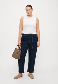 Top alb fără mâneci, pantaloni din denim cu talie înaltă de culoare albastru închis, geantă bej și pantofi plată de culoare maro deschis. Design simplu, croială confortabilă.