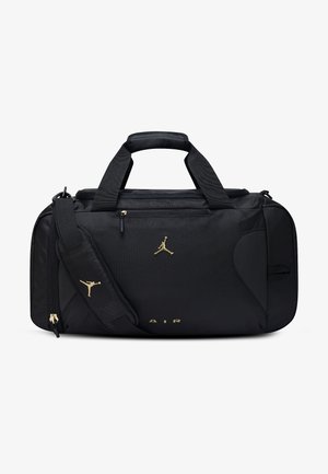 Bolsa duffel negra con logo Jumpman dorado, asas superiores, correa de hombro ajustable, bolsillo frontal con cremallera y texto "AIR" en el centro inferior.