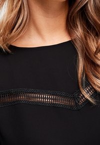 Prenda negra con un panel de encaje detallado en el escote, con una textura suave y una silueta clásica.