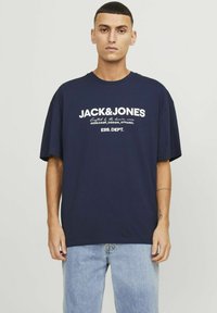 Camiseta de algodón de gran tamaño en azul marino con un diseño de logotipo y texto en blanco en el pecho, cuello redondo y mangas cortas.