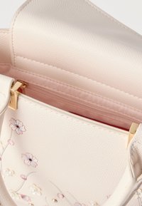 Petit sac à main rose poudré avec broderies florales, détails en perles et fermoir doré, présenté ouvert pour révéler une poche intérieure zippée.