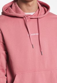 Felpa con cappuccio rosa in cotone con tasca a marsupio, cappuccio con coulisse con terminali argentati e logo bianco sul petto.