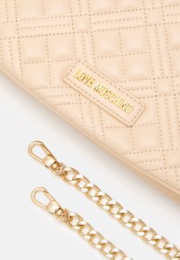 Prošívaná béžová syntetická kabelka se zlatými doplňky, s destičkou s logem "LOVE MOSCHINO" a odnímatelným zlatým řetízkovým popruhem.