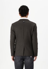 Donkergrijze blazer met een notch-kraag, enkele split en knoopmanchetten. Voorzien van een logodetail op de achterkant en een textuurstof.