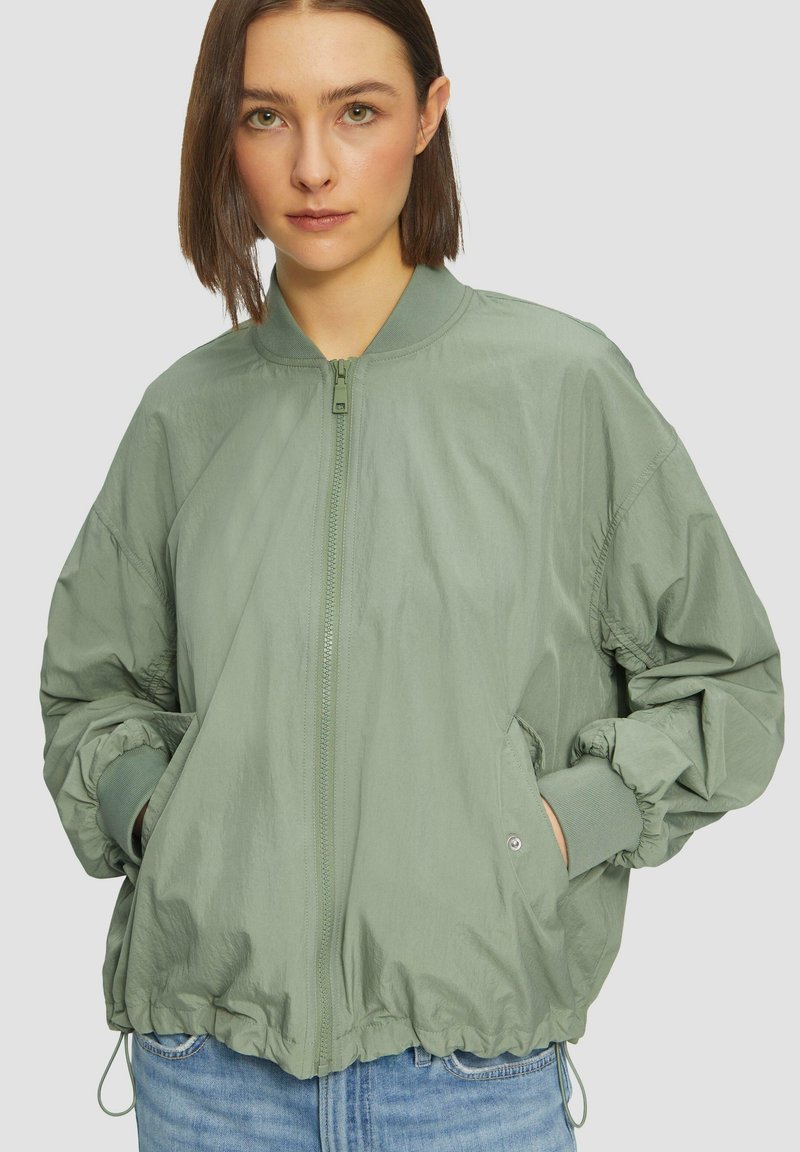Hellgrüne Bomberjacke mit Reißverschluss vorne, elastischen Bündchen und Kordelzug am Saum. Verfügt über zwei Seitentaschen und eine glatte Textur.