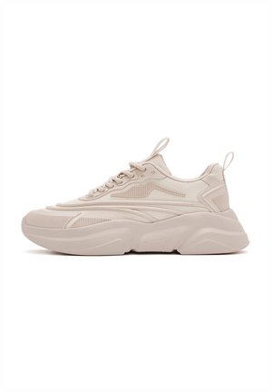 Beige Sneaker mit einem strukturierten Mesh-Obermaterial, solider Gummisohle und geschwungenem Design. Enthält Schnürsenkel, Zuglasche und markante Seitenstreifen.