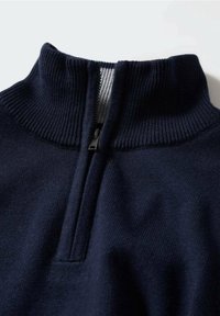 Pull en maille bleu marine avec un col montant côtelé et une petite fermeture éclair partiellement ouverte, laissant apparaître une doublure intérieure grise.