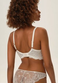 Biały komplet koronkowej bielizny z delikatnym wzorem kwiatowym, regulowanymi ramiączkami oraz zapięciem na haftkę z tyłu. Miękkie kwiatowe akcenty podkreślają projekt.