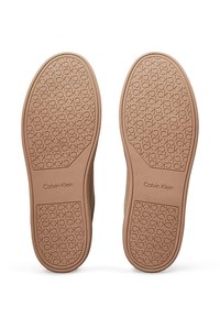 Soli in gomma marrone con motivo del logo CK. Texture liscia, forma arrotondata e etichettatura discreta sul lato indicano l'identità del marchio.