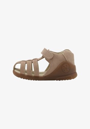 Sandale en daim beige avec un design à bout ouvert, plusieurs fermetures à lanières et une semelle en caoutchouc arborant un logo sur le talon.