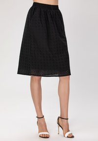 Jupe noire mi-longue avec une taille élastique, ornée d'un motif brodé et de découpes à œillets le long de l'ourlet. Texture lisse.