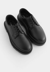 Chaussures en cuir noir avec une finition lisse, bout arrondi, design à lacets et semelle en caoutchouc texturée. Style minimaliste sans accents supplémentaires.