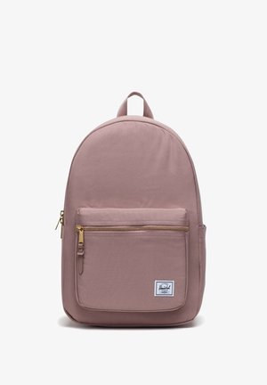 Sac à dos en tissu rose avec une forme arrondie, une poche zippée à l'avant et un écusson de logo blanc. Il dispose d'une poignée supérieure et de bretelles rembourrées réglables.
