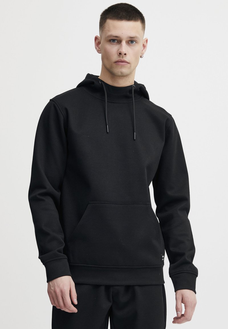Svart hettegenser med kengurulomme, snor i hetta, ribbestrikkede mansjetter og strukturert stoff. Enkel, minimalistisk design.