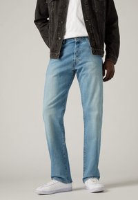 Jeans in denim blu chiaro con un taglio dritto, sezioni sbiadite e un classico design a cinque tasche, indossati con una maglietta bianca e un giubbotto nero.