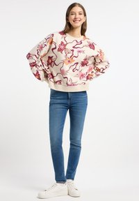 Crèmekleurige sweatshirt met een bloemmotief in roze en oranje tinten, ruime mouwen en een geribbelde zoom. Gepaard met blauwe skinny jeans en witte sneakers.