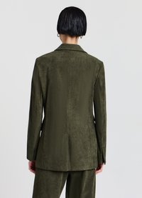 Blazer en velours côtelé vert olive avec un col cranté, des manches longues et une texture à côtes verticales. Présente une fente centrale au dos pour plus de liberté de mouvement.