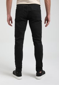 Jeans neri slim fit con tasche posteriori, una texture sbiadita e una cintura. Abbinati a scarpe da ginnastica nere con suole bianche.