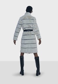 Kabát z umělé kožešiny světle šedý s černými pruhy, s páskem v pase. Délka ke kolenům s dlouhými rukávy, doplněný černými kozačkami ke kolenům.