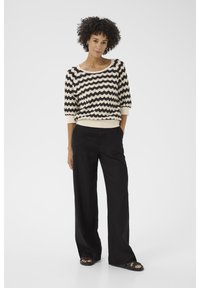 Maglione a righe nere e crema con motivo a onda, scollo ampio e maniche a tre quarti, abbinato a pantaloni neri larghi.