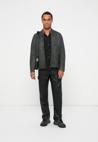 Chaqueta de cuero negra con un acabado texturizado sutil, combinada con una camisa oscura y pantalones de cuero. Los accesorios incluyen un bolso negro de hombro.