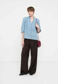 Šviesiai mėlyna džinsinė marškeliai su raukšlėta apykakle ir sagutėmis, derinami su laisvomis rudos spalvos kelnėmis. Neša mažą bordo spalvos kryžminį maišelį ir juodus batus.