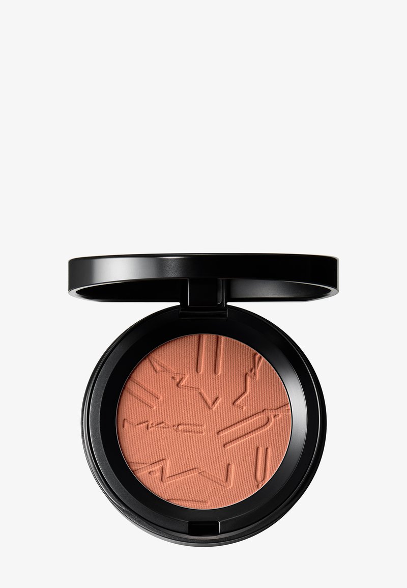 Étui à maquillage noir compact ouvert révélant une poudre pressée ton pêche avec un motif abstrait embossé sur fond blanc.