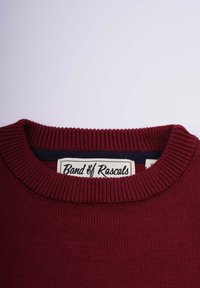 Bordeauxtröja med en strukturerad ribbad stickning, rund halsringning och en etikett som visar "Band of Rascals" i en kontrasterande vit text.